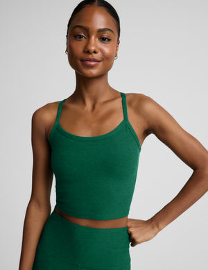 Woman wearing a green cropped racerback tank and leggings against a plain background. 
