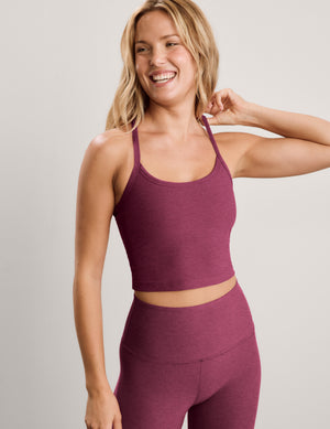 A smiling blonde woman wearing a matching heathered mauve activewear set, featuring a scoop-neck crop top and high-waisted leggings, against a solid light gray studio background.