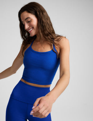 A woman modeling a bright royal blue activewear set, featuring a scoop-neck crop top and matching high-waisted leggings, against a solid light gray background.