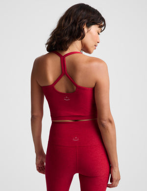 A woman wearing a matching red activewear set consisting of a cropped tank top and high-waisted leggings, photographed against a light gray studio background.