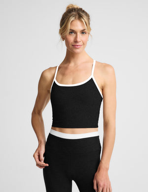 A woman modeling a black cropped tank and matching black leggings with white trim, photographed against a light gray studio background.