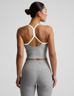 A woman shown from the back wearing a heather gray sports bra with white trim and matching heather gray leggings against a light gray studio background.