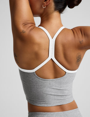 Rear view of a woman wearing a heather gray cropped tank with a white crisscross back strap design, against a light gray studio background.