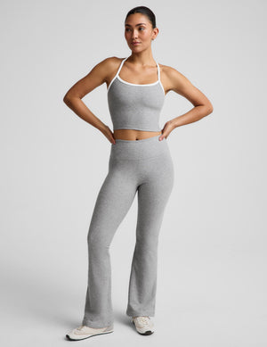 A woman modeling a light gray heather matching loungewear set consisting of a cropped tank top with white trim and high-waisted flared pants, standing against a light gray studio background.