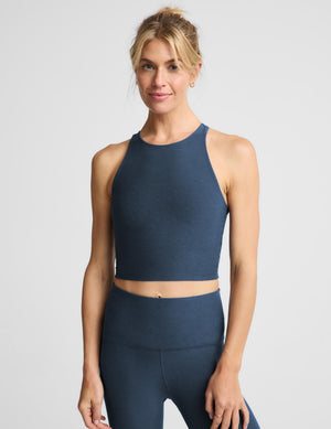 A woman modeling a matching athletic set consisting of a dark blue-gray halter crop top and high-waisted leggings, photographed against a light gray studio background.