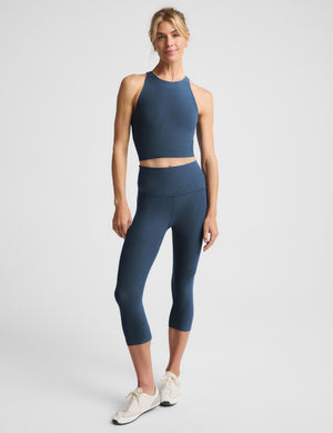 A woman modeling a matching athletic set consisting of a dark blue-gray halter crop top and high-waisted leggings, photographed against a light gray studio background.