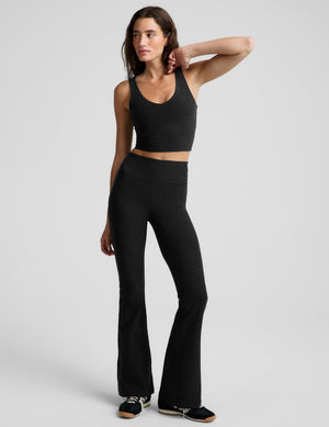 A woman modeling a black scoop-neck athletic crop top and matching black leggings against a light gray studio background.