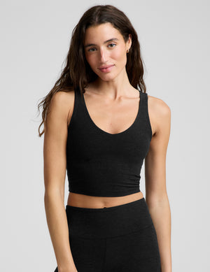 A woman modeling a black scoop-neck athletic crop top and matching black leggings against a light gray studio background.