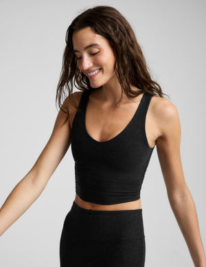A woman modeling a black scoop-neck athletic crop top and matching black leggings against a light gray studio background.