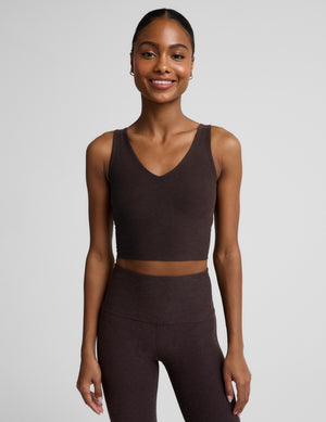 Woman wearing a brown cropped v-neck tank top and brown bootcut pants against a plain background. 