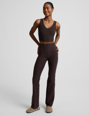 Woman wearing a brown cropped v-neck tank top and brown bootcut pants against a plain background. 
