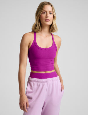 Woman wearing a purple cropped racerback tank top and purple sweatpants against a plain background. 