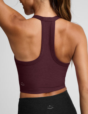 A woman modeling a scoop-neck athletic tank top in deep burgundy, paired with black athletic pants, against a solid light gray background.