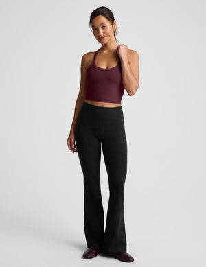 A woman modeling a scoop-neck athletic tank top in deep burgundy, paired with black athletic pants, against a solid light gray background.