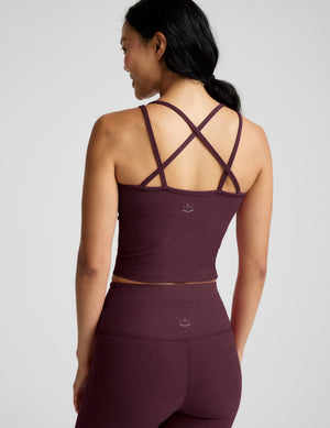 Rear view of a woman wearing a matching burgundy activewear set, featuring a tank top with crisscross back straps and high-waisted leggings, against a light gray studio background.