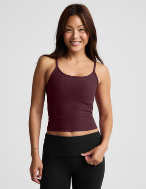 A woman modeling a dark burgundy spaghetti-strap tank top and black pants against a light gray studio background.
