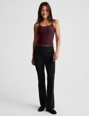 A woman modeling a dark burgundy spaghetti-strap tank top and black pants against a light gray studio background.