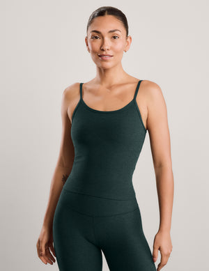 A woman modeling a dark forest green athletic tank top and matching high-waisted pants against a light gray studio background.