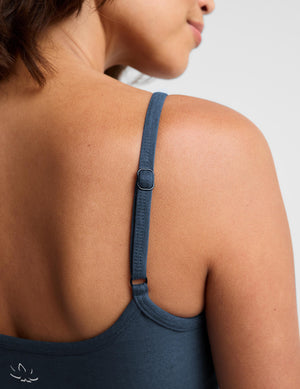 A woman modeling a dark slate blue camisole tank top and matching leggings against a light gray studio background.