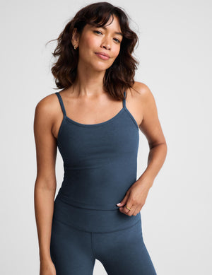 A woman modeling a dark slate blue camisole tank top and matching leggings against a light gray studio background.