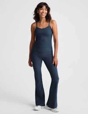 A woman modeling a dark slate blue camisole tank top and matching leggings against a light gray studio background.
