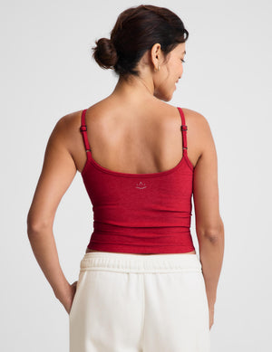 A woman shown from the back wearing a red spaghetti-strap tank top and white sweatpants against a light gray studio background.