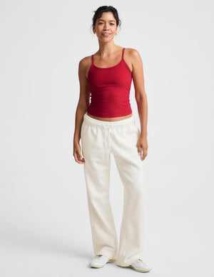 A woman modeling a red tank top and off-white wide-leg sweatpants against a light gray studio background.