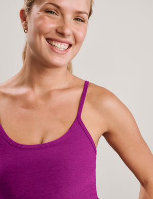 A woman modeling a bright magenta-purple tank top and matching high-waisted leggings against a light gray studio background.