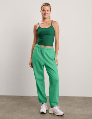 Woman wearing a green waist length tank and green sweatpants against a plain studio background. 