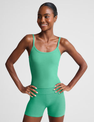 A woman modeling a bright green tank and matching green shorts against a light gray studio background.