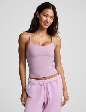A woman modeling a light purple/lavender ribbed camisole crop top and matching sweatpants against a light gray studio background.
