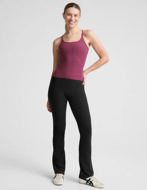 A woman modeling a heathered magenta racerback tank top paired with black leggings, photographed against a solid light gray studio background.