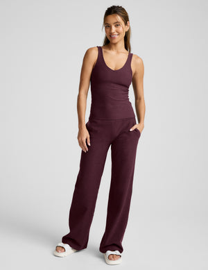 A woman modeling a matching two-piece active set in a deep red color, consisting of a sleeveless scoop-neck tank top and wide-leg pants, photographed against a neutral light gray background.