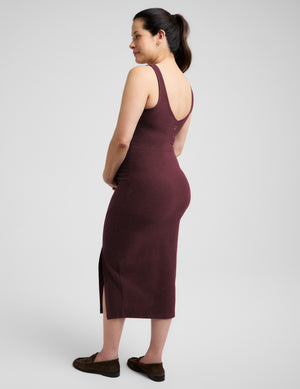 Pregnant woman wearing a red maternity dress and brown loafers against a plain studio background. 