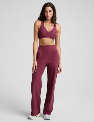 A woman modeling a heathered burgundy sports bra and matching high-waisted pants against a light gray studio background.