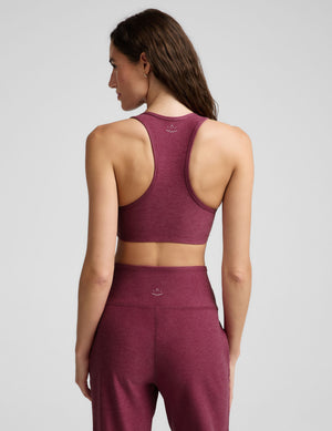 A woman modeling a heathered burgundy sports bra and matching high-waisted leggings against a light gray studio background.