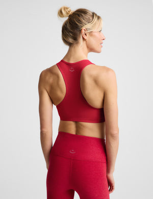 A woman modeling a bright red sports bra and matching red leggings against a light gray studio background.