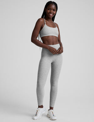 Woman wearing a gray sports bra and leggings on a light gray background. 