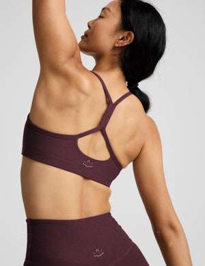 A woman modeling a matching athletic set consisting of a scoop-neck sports bra and high-waisted leggings in a deep red color, shot against a solid light gray background.