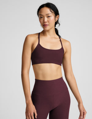 A woman modeling a matching athletic set consisting of a scoop-neck sports bra and high-waisted leggings in a deep red color, shot against a solid light gray background.