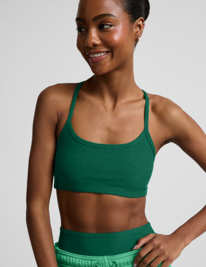 Woman wearing a green sports bra and green biker shorts with light green sweatpants on top against a plain background. 