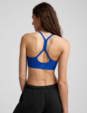 A woman wearing a bright royal blue athletic sports bra and black sweatpants, posing against a light gray studio background.