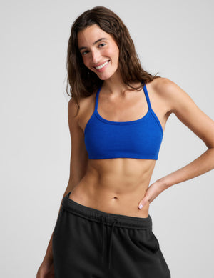 A woman wearing a bright royal blue athletic sports bra and black sweatpants, posing against a light gray studio background.