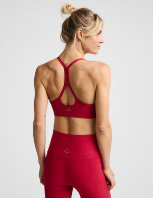 A woman modeling a bright red sports bra and matching high-waisted leggings against a light gray studio background.