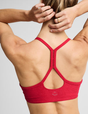 A woman modeling a bright red sports bra and matching high-waisted leggings against a light gray studio background.