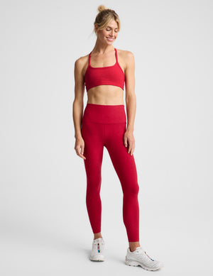 A woman modeling a bright red sports bra and matching high-waisted leggings against a light gray studio background.