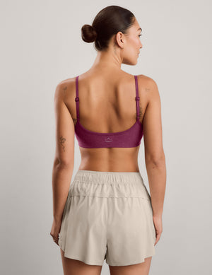 A woman modeling a heathered red purple sports bra and light beige athletic shorts against a solid light gray studio background.