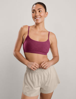 A woman modeling a heathered red purple sports bra and light beige athletic shorts against a solid light gray studio background.