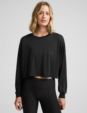 Woman wearing a black long sleeve top and leggings against a plain studio background. 