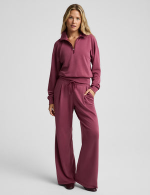 A woman modeling a matching dusty rose half-zip sweatshirt and drawstring sweatpants set against a solid light gray background.